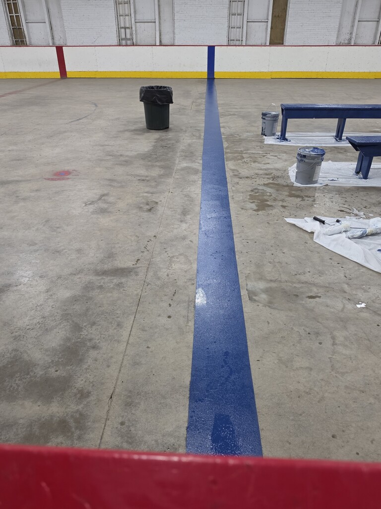 A freshly painted blue stripe on the concrete of a rink.