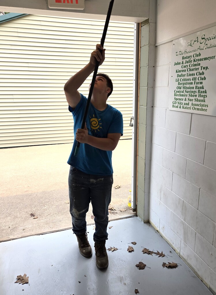 A student sweeps spider webs off the ceiling with a broom.