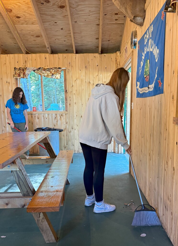 Two students sweep the floor of a camp building.