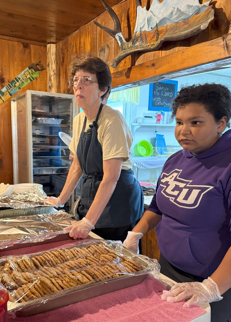 An adult and a student stand ready to pass out food in a line.