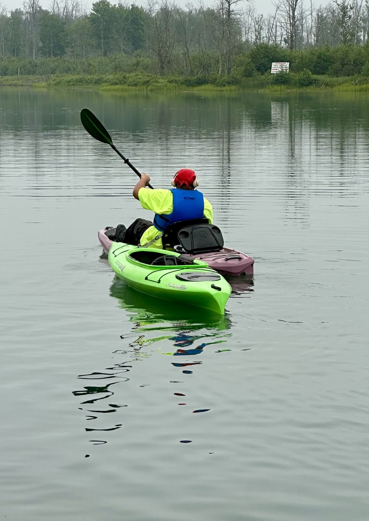 A picture from behind of a student kayaking on smooth water. He is towing another kayak behind him.