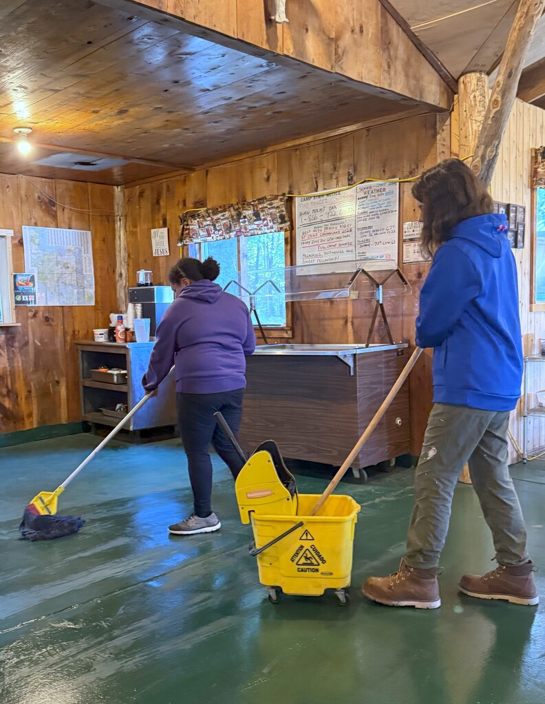 Two students mop a dark green camp floor.