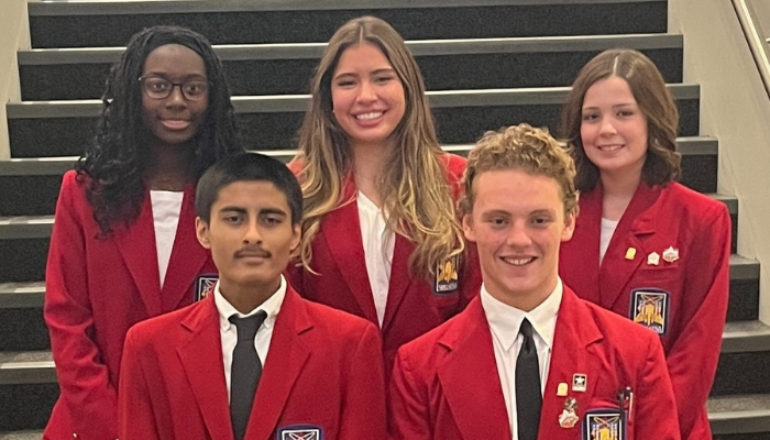 A group of five SkillsUSA students stand on a staircase wearing red SkillsUSA blazers, white shirts, and black ties. Two students stand in the front row and three stand behind them. All are smiling and facing the camera.