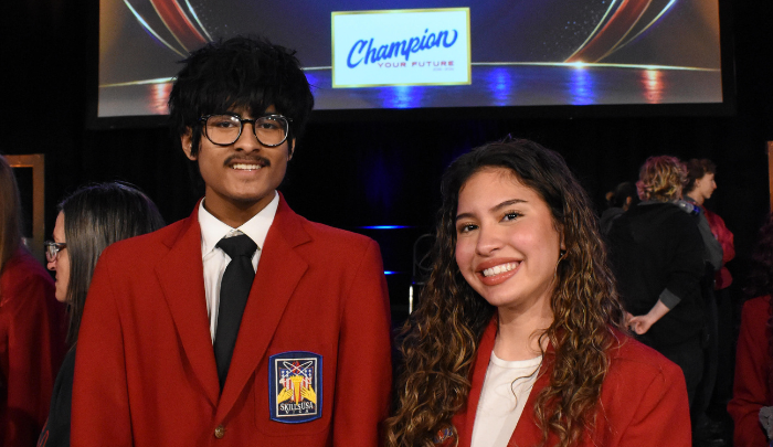 Two Eastland-Fairfield students wearing red SkillsUSA blazers pose together at an event after being selected as SkillsUSA State Officers. They are smiling in front of a stage backdrop with a “Champion Your Future” display.