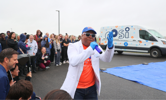 Dr. Frederic Bertley, president and CEO of COSI, speaks to a crowd of students outdoors during the 2026 COSI Science Festival kickoff at Fairfield Career Center, with a COSI van parked in the background.