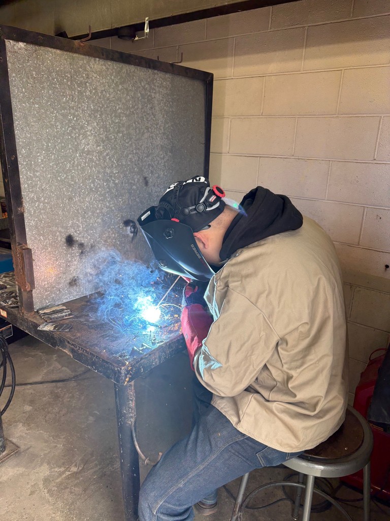 man in brown and black sweatshirt wearing welding helmet welding a project on a welding table