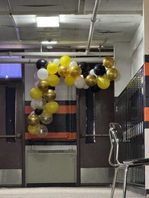 gold, yellow, white, and black balloons create an arch above a doorway