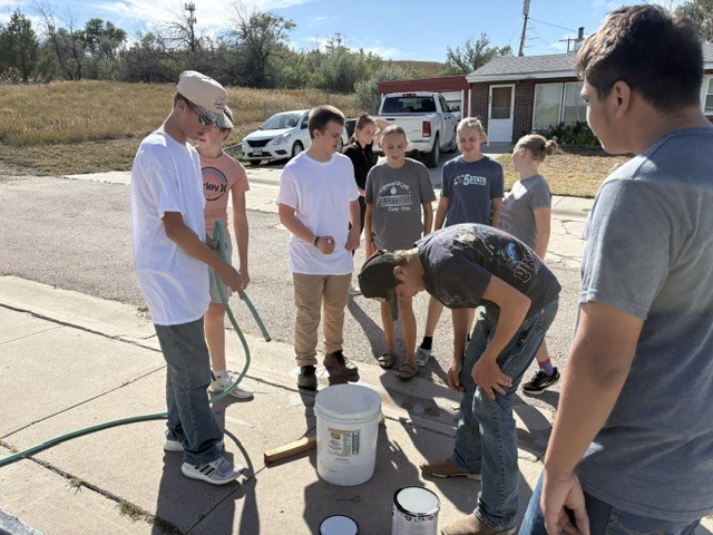 students standing in a circle, mixing paint in a white bucket