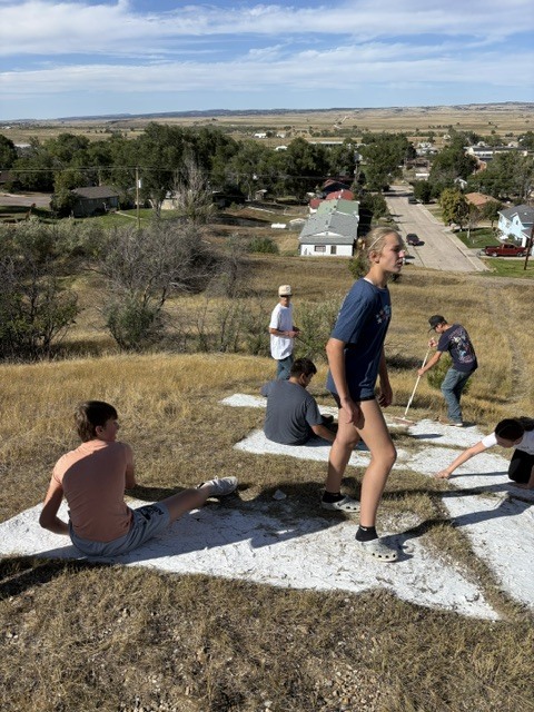 students using white paint to design an E on a hill overlooking a town street