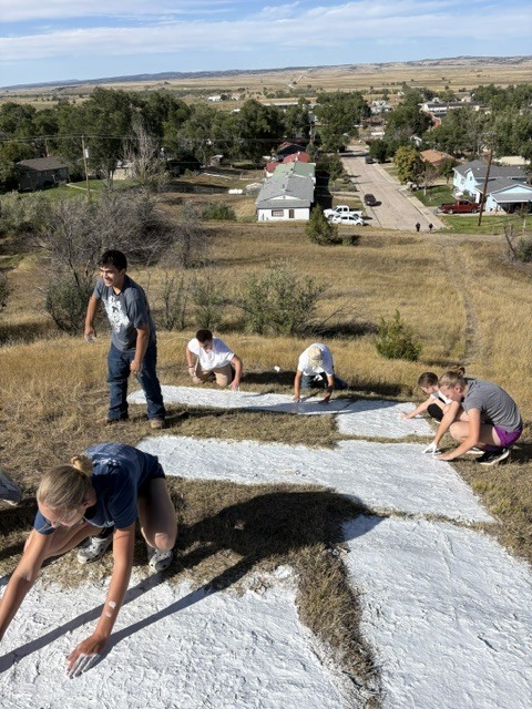 students using white paint to stencil a large E on a hill overlooking town streets