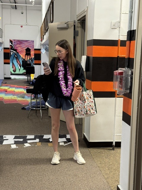 teacher ready to hit the beach wearing a lei, holding a phone, a Stanley, and a beach bag
