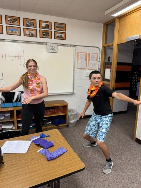 Students wearing leis posing in hula dance pose and surfing pose