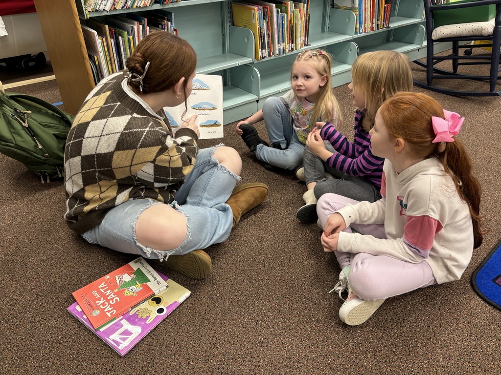 EHS studnet sitting on the floor with 3 EECC students reading them a story 