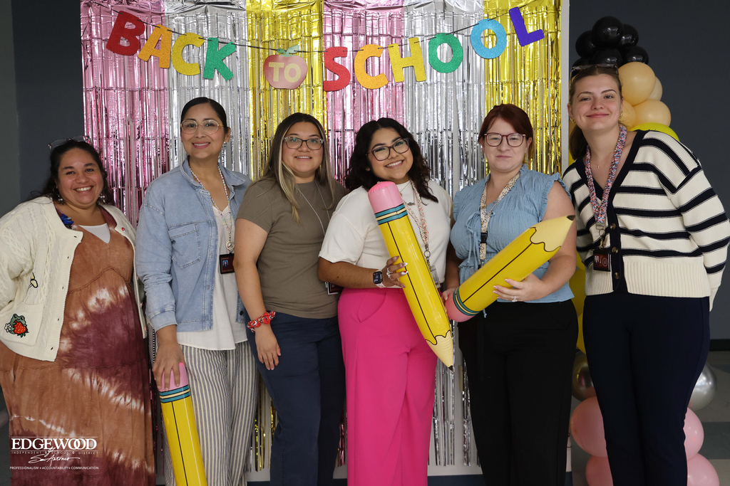 new teachers pose for a photo together infront of a Back to School backdrop