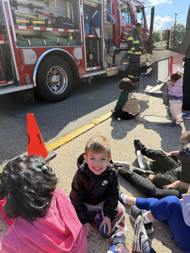 Young preschool boy smiling with a red fire truck behind him