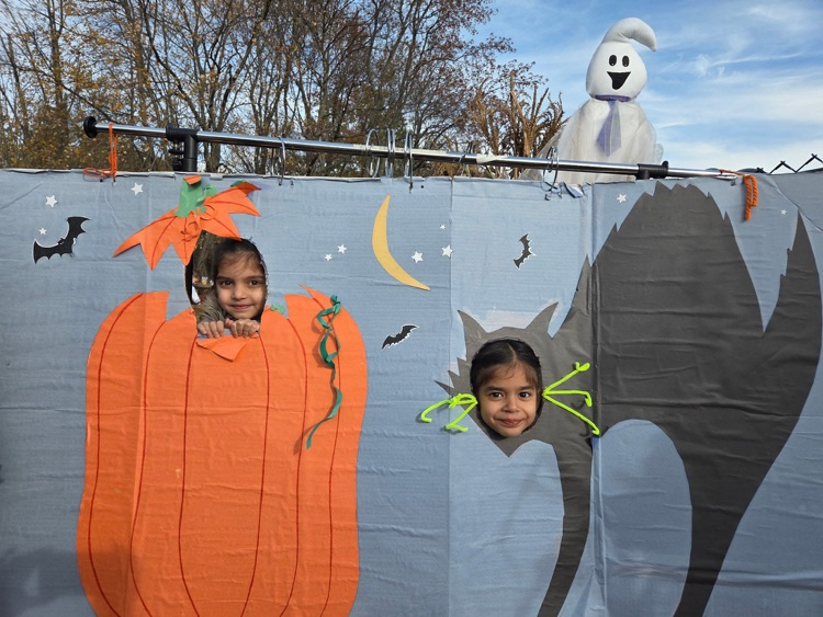 two young children with their heads in a pumpkin cutout and a cat face cut out
