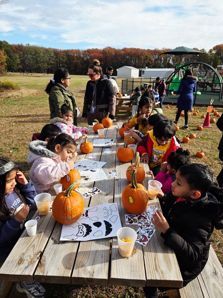 Young children sitting at a long table, decorating pumpkins