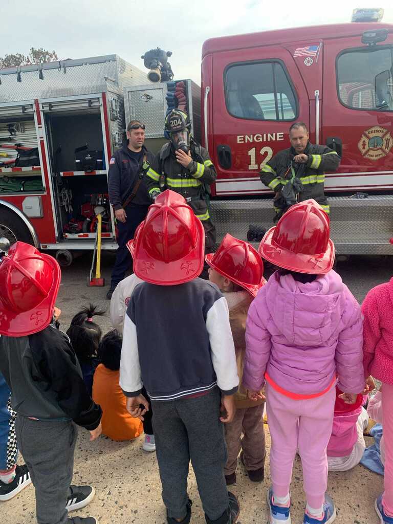 Preschoolers in red fire helmets looking at a fire truck