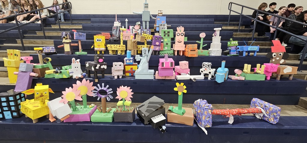 3D creations sitting on the gym bleachers with students sitting off to the sides