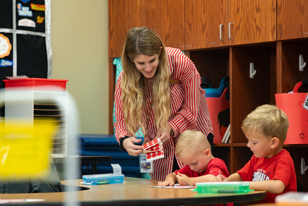 teacher helping a pre schooler work on a craft at their table
