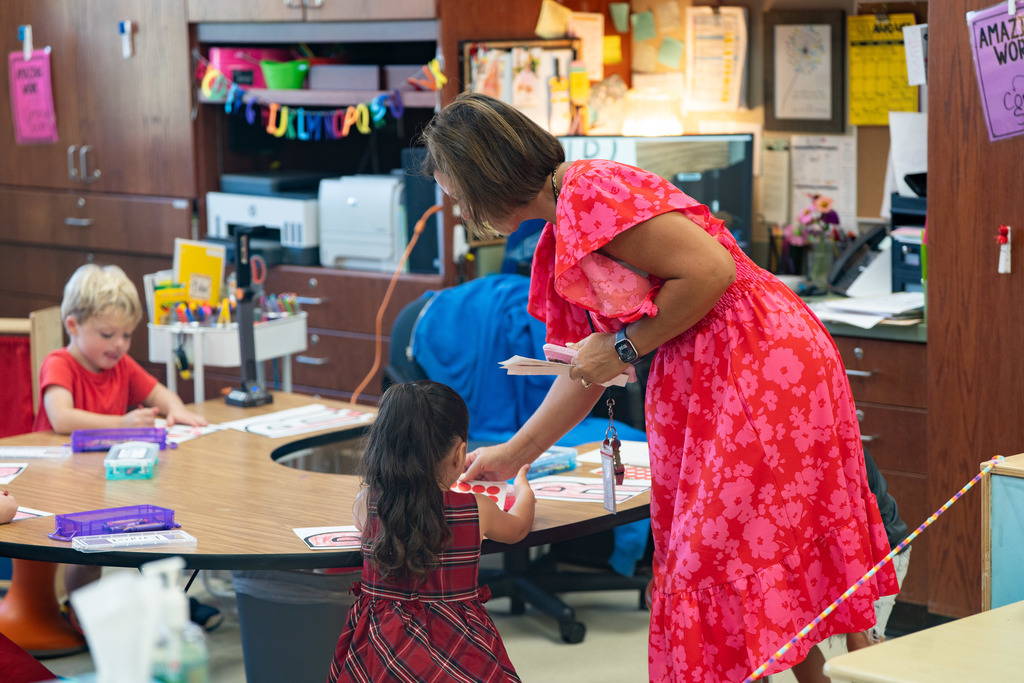 teacher helping a pre schooler work on a craft at their table