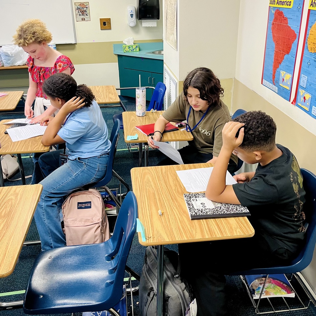 Students sitting in desks review answers on their social studies assignment to wrap up a lesson on absolute and relative location.