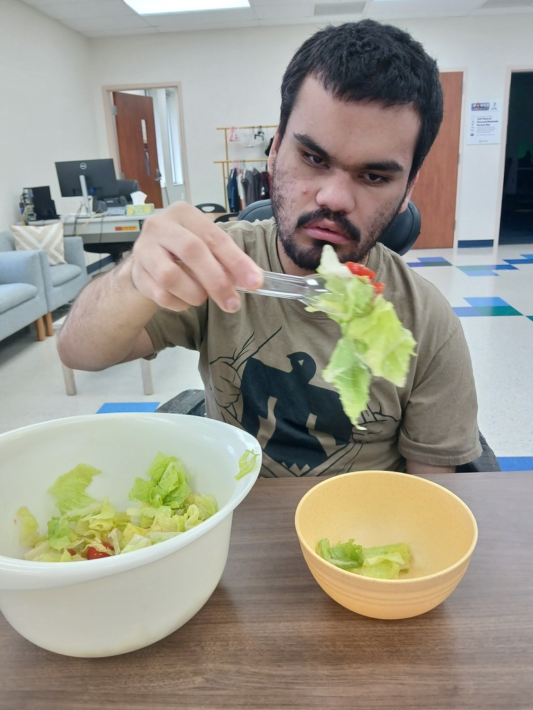 an intern using tongs to put salad in a serving bowl