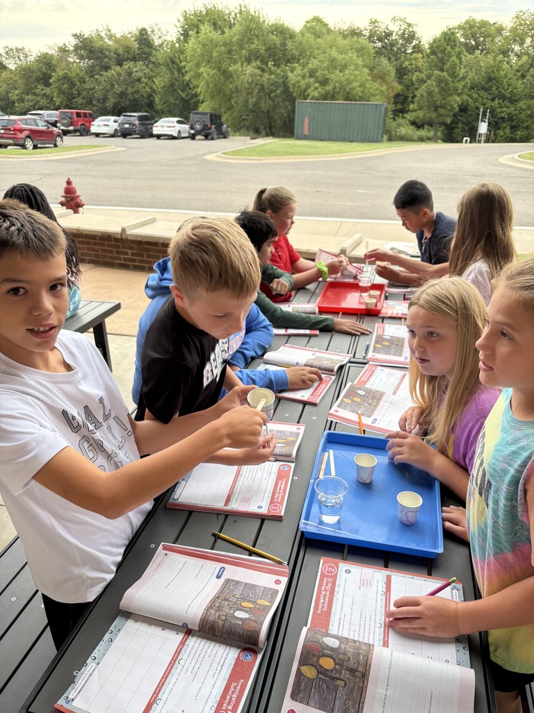 Kids sitting at a table outside reading from workbooks