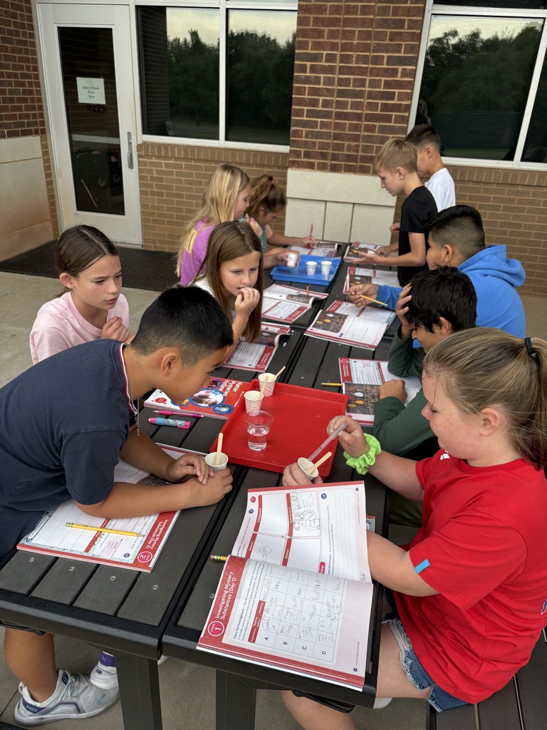 Kids sitting at a table outside reading from workbooks