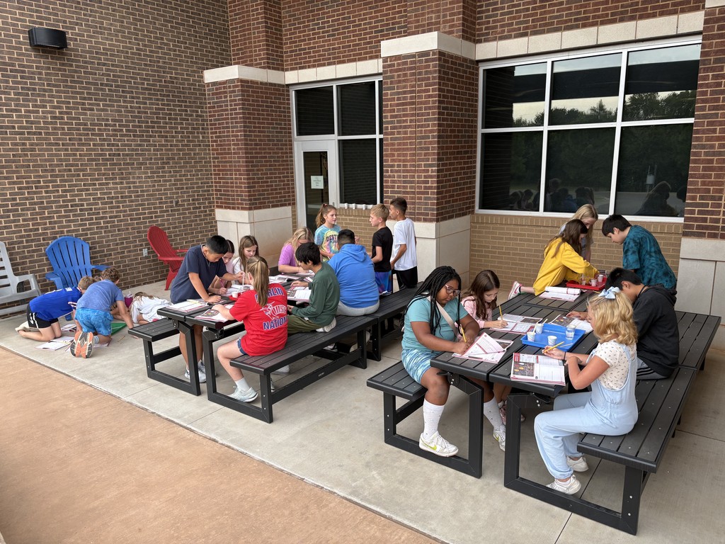 Kids sitting at a table outside reading from workbooks
