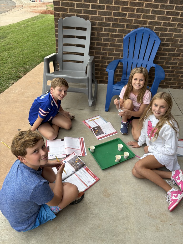 Kids sitting at a table outside reading from workbooks
