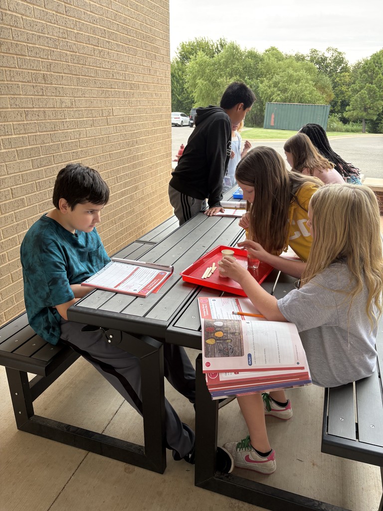 Kids sitting at a table outside reading from workbooks