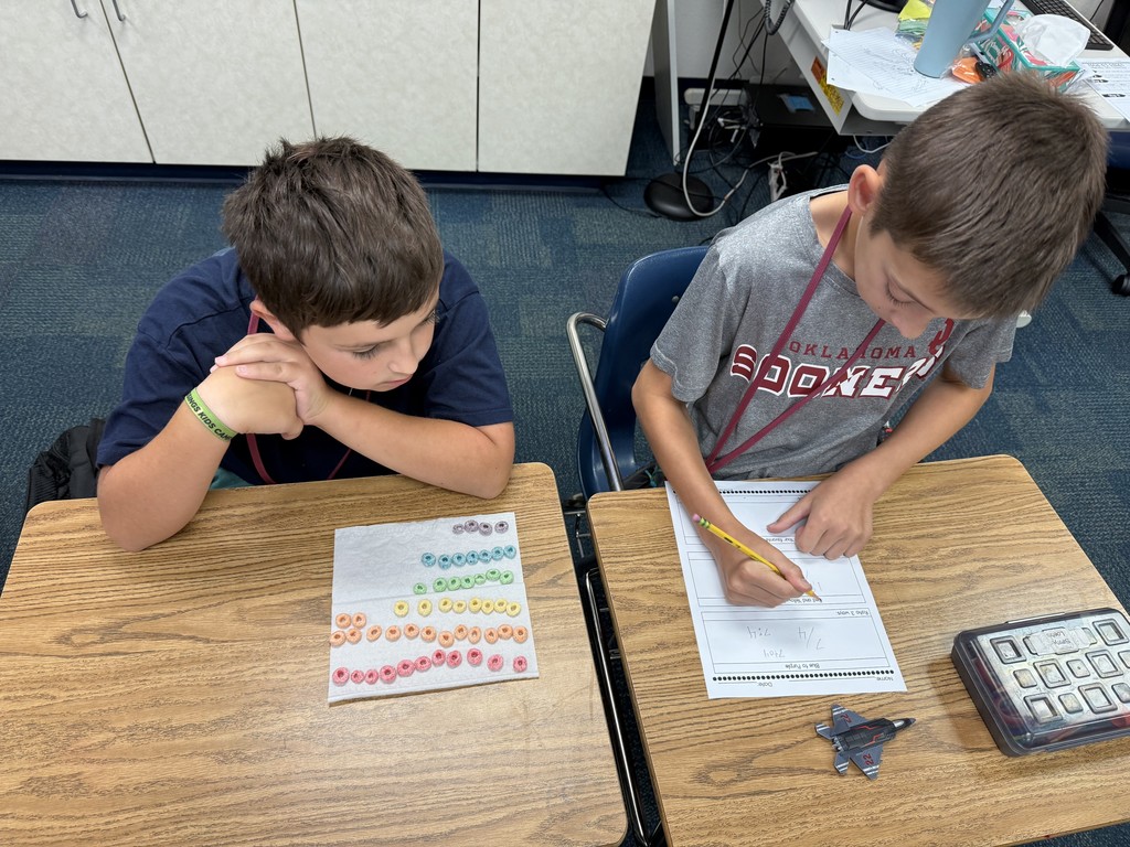 2 students looking at a worksheet with Fruit Loop cereal grouped by colors sitting on the desk beside them.