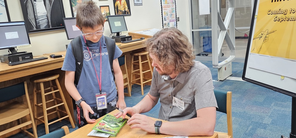 A boy talking with author Nathan Hale after he finished autographing a book. The front cover of Bones and Berserkers is on display