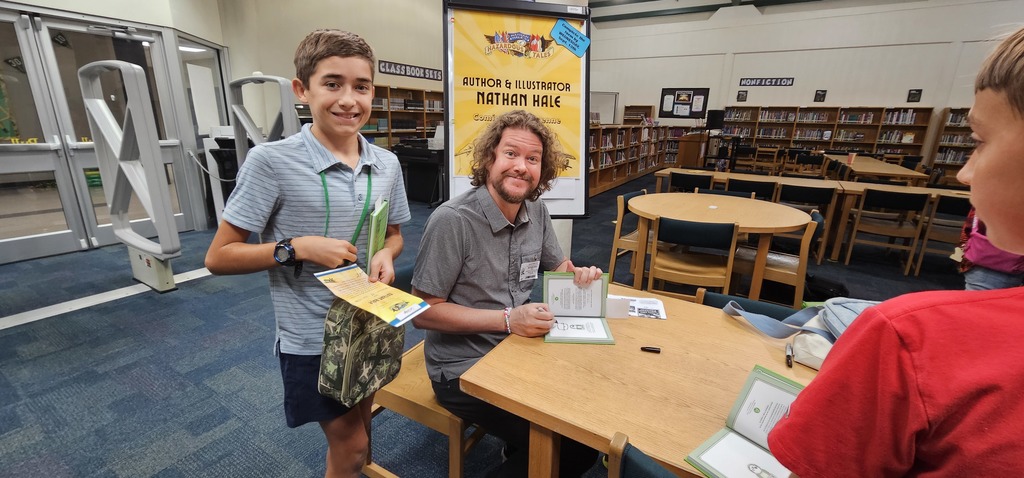 A male student and author, Nathan Hale, smiling for the camera. Nathan Hale is autographing a book