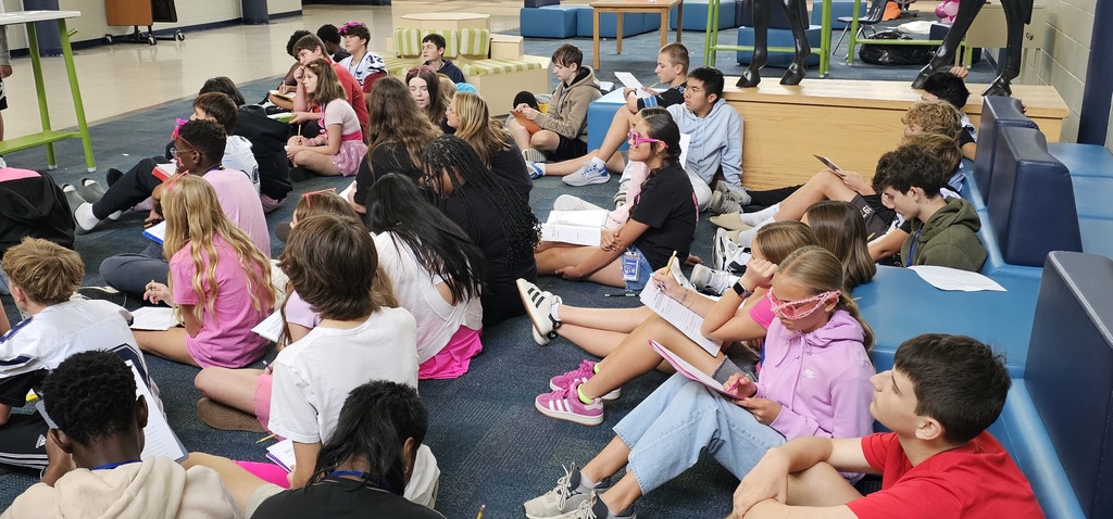 A group of students sitting on the floor in the commons with a worksheet in the lap and pencil in their hands