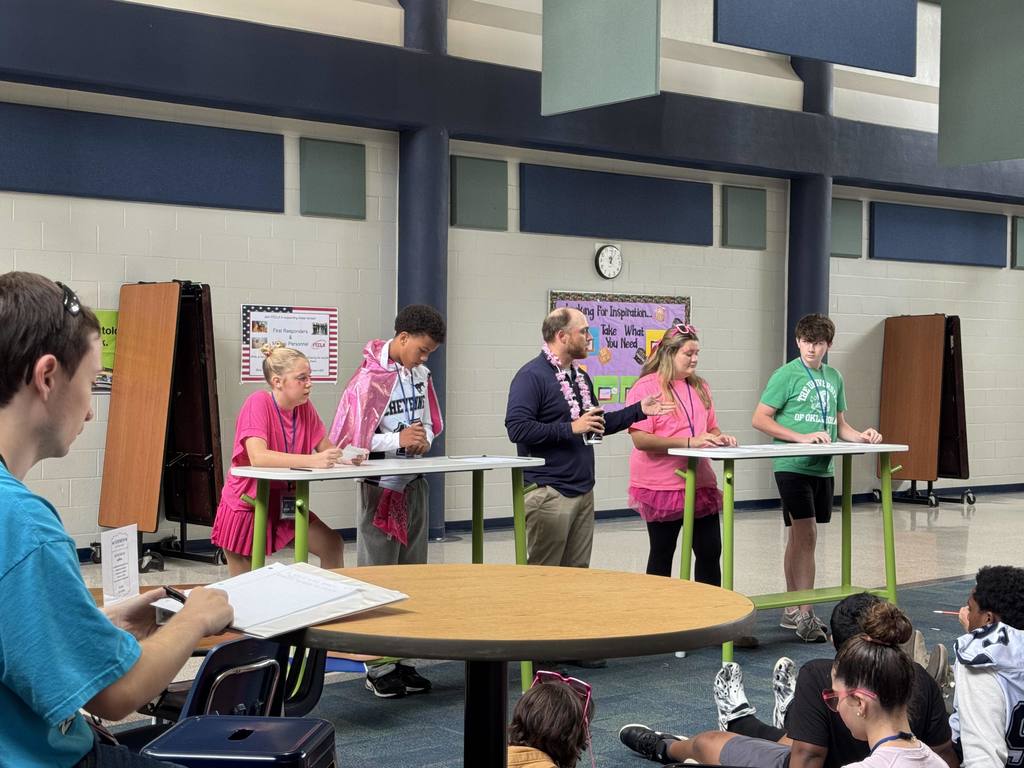 Two tables with a boy and a girl at each table with a teacher standing between them giving instructions