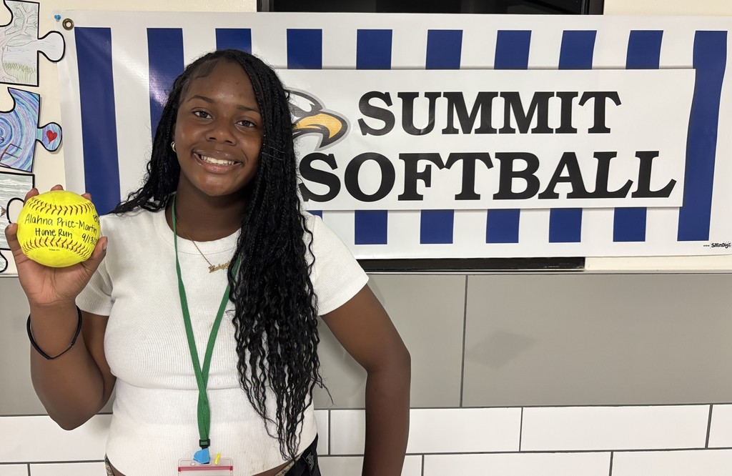 Lady Eagle, Alahna, poses next to a Summit Softball sign with her home run softball!