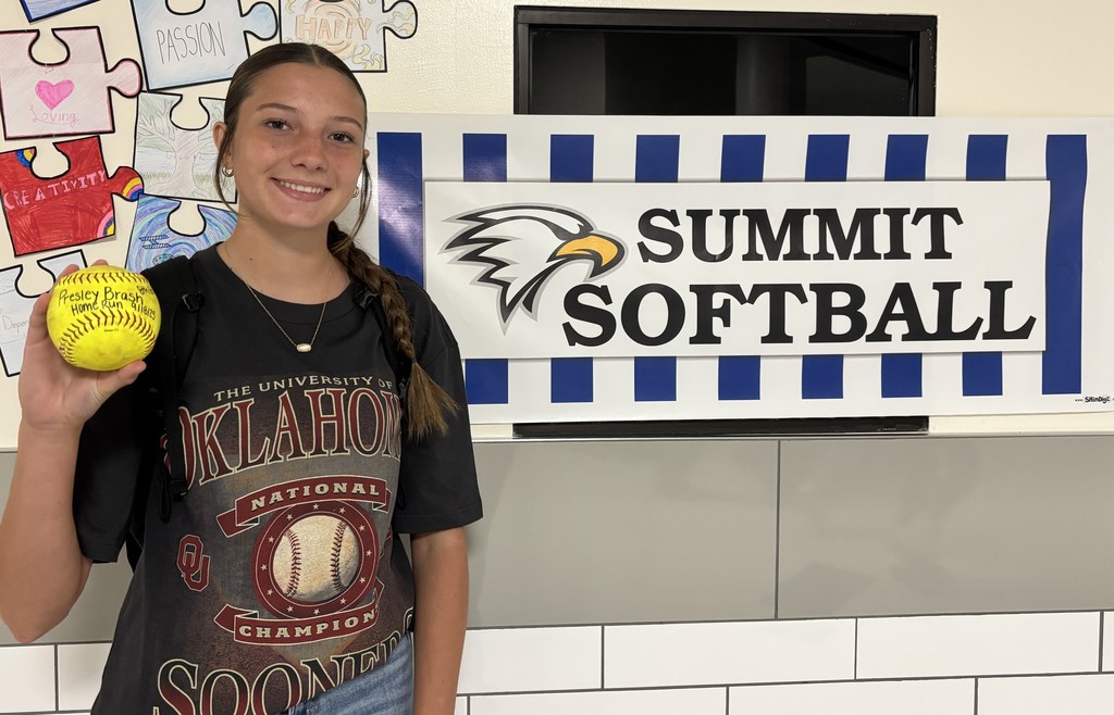 Lady Eagle, Presley, poses next to a Summit Softball sign with her home run softball!