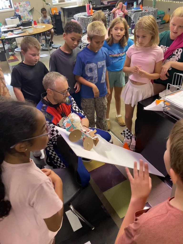 teacher surrounded by students dropping egg crash car down a ramp