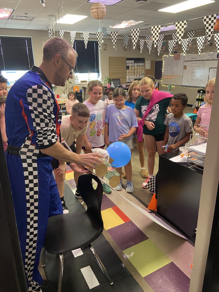 teacher surrounded by students dropping egg crash car down a ramp