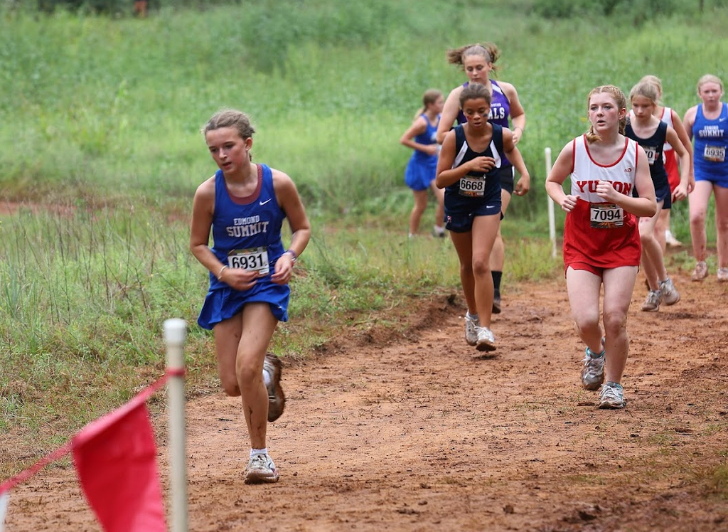 Girl cross country athletes run on a muddy track at a meet.