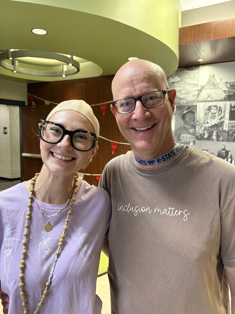 Two people smile, one wearing a bald cap
