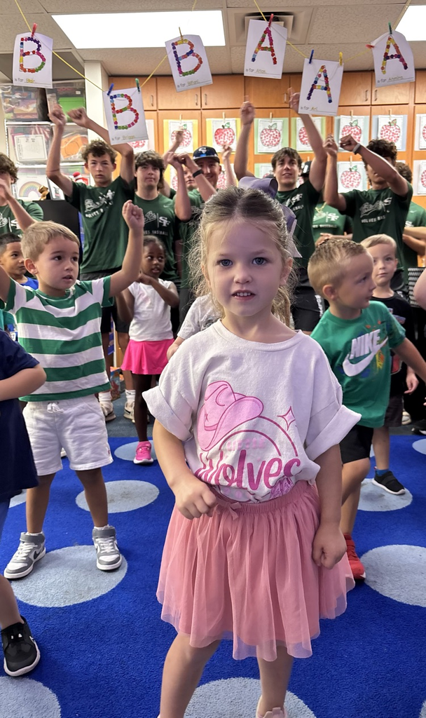 pre-K student doing a song and dance with high school kids in the background 
