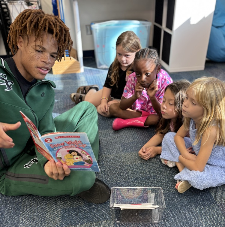 high school basketball player reading a princess story to a group of first grade girls 