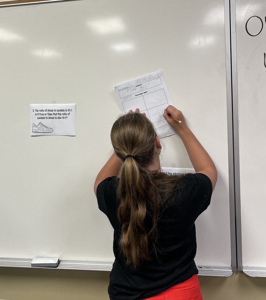 Student writes on paper that is being held to the wall as she completes a math review activity.