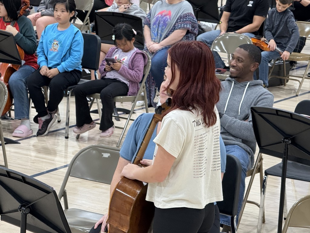 A teenage girl holding a cello with families sitting in chairs in the background