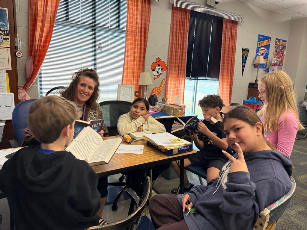 Kids and teacher with books sitting around a table.