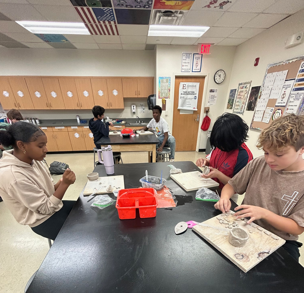 Students sit in a group at a table as they work on their clay pinch pot projects.
