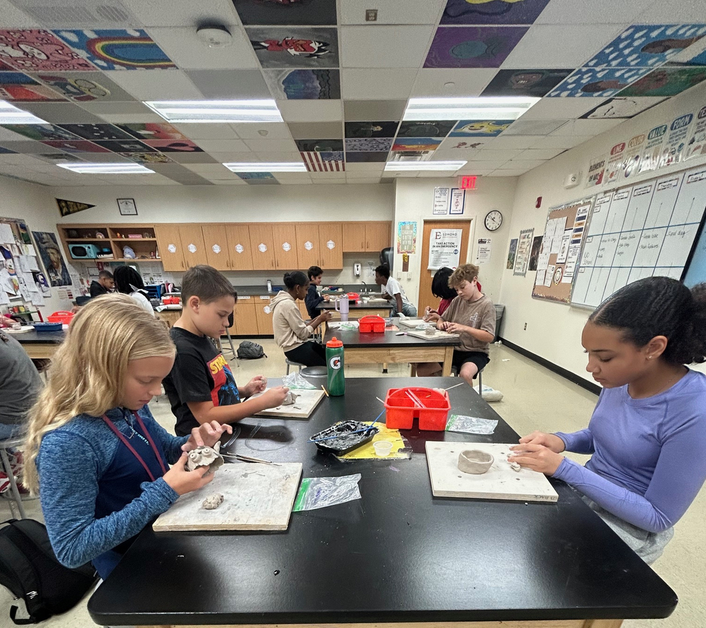 Students sit in a group at a table as they work on their clay pinch pot projects.
